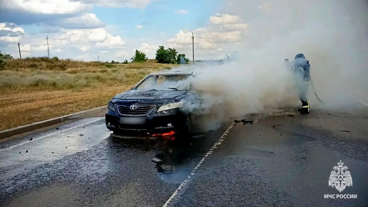 Сотрудник МЧС тушит горящий гражданский автомобиль на дороге