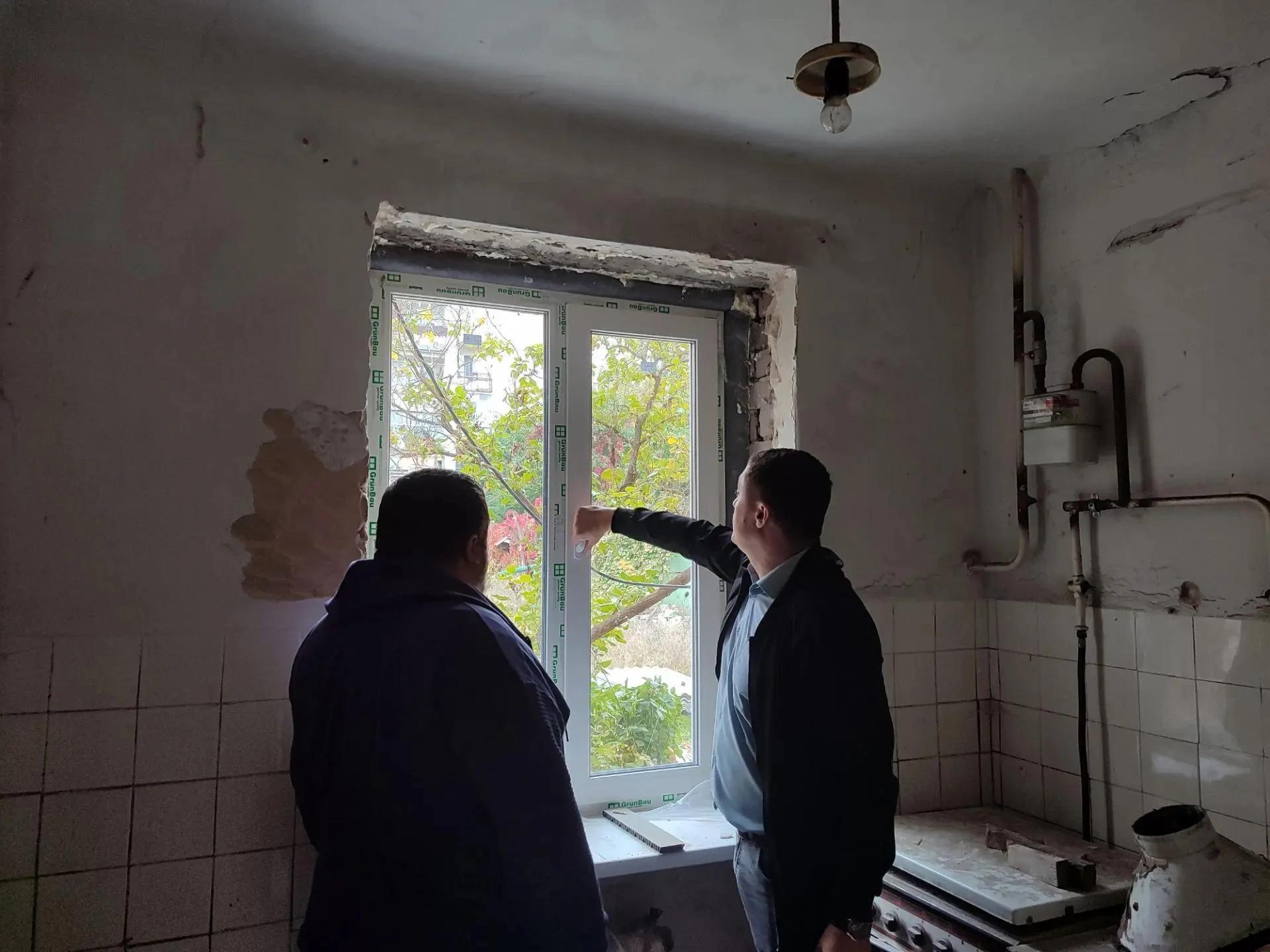 Двое мужчин у установленного белого окна в помещении с незавершённой отделкой