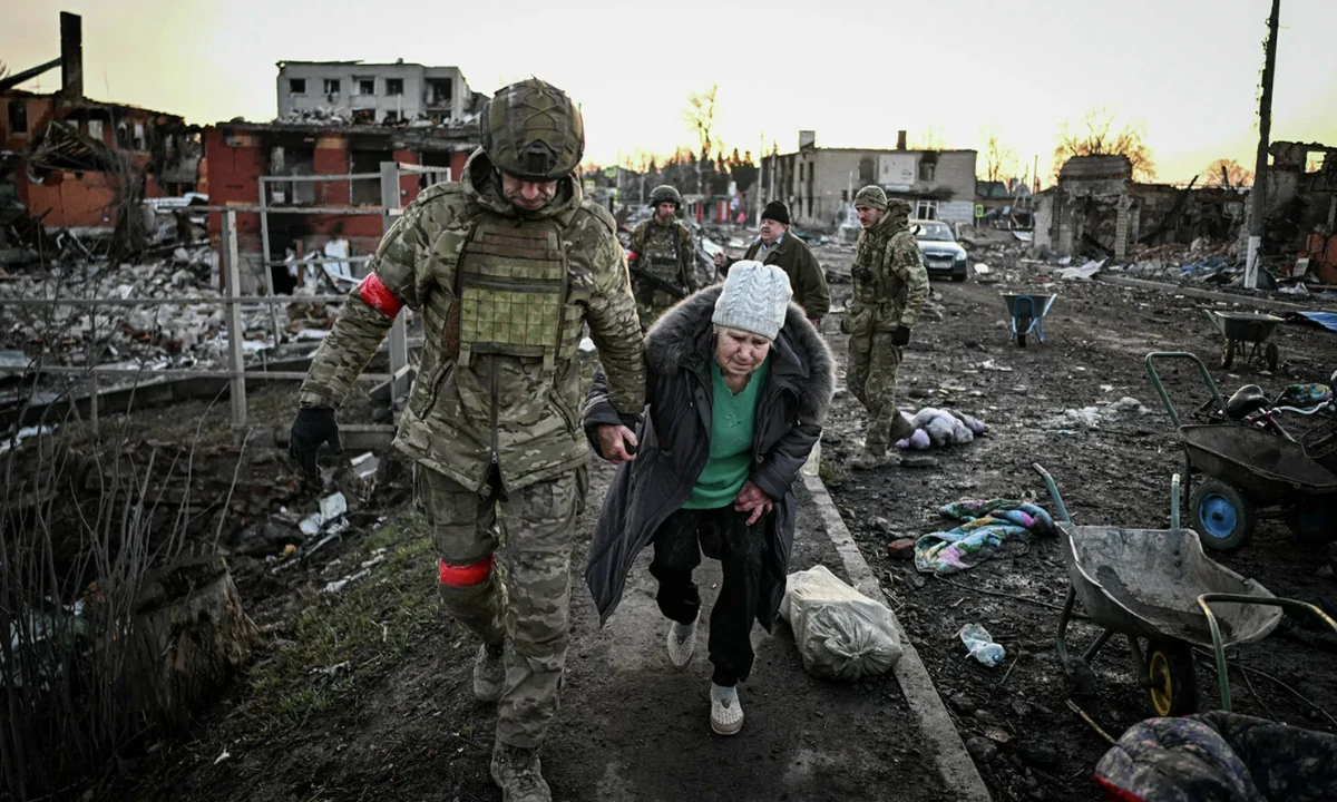 Военнослужащий помогает пожилой женщине пройти через разрушенный район во время эвакуации